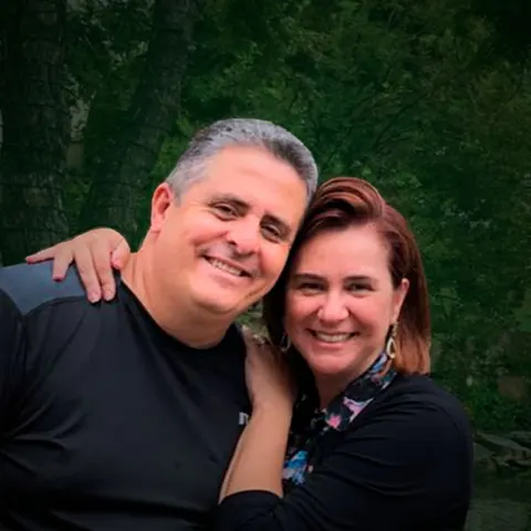 Apóstolo Adriano José e Apóstola Daniela Camargo abraçados e sorrindo, com árvores ao fundo